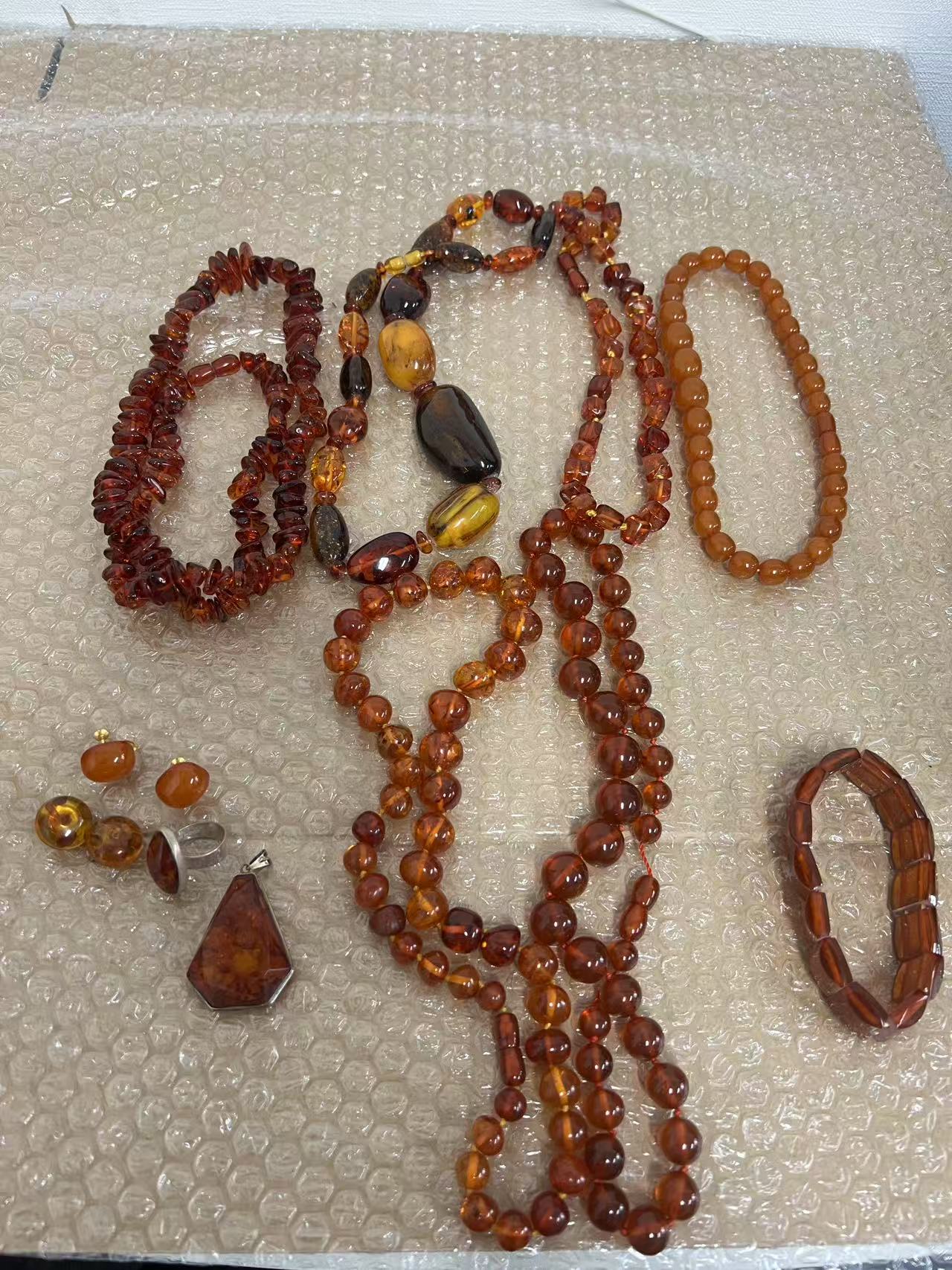 多款琥珀饰品平铺展示,包括项链、耳钉和手串,色泽从浅黄到深蜜色。