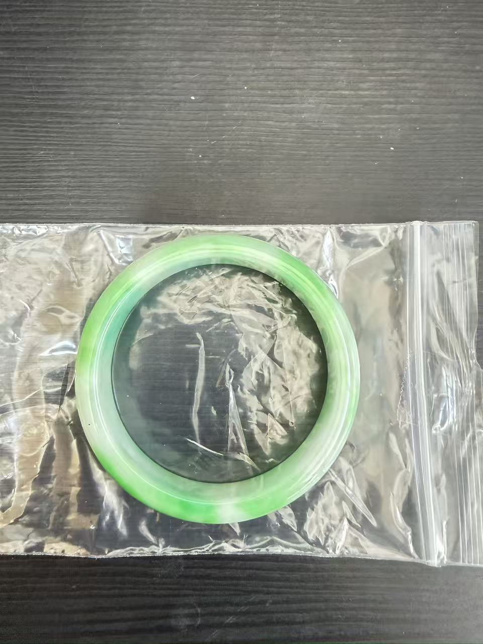 日本代拍玉镯实物图，玉镯置于透明密封袋中，呈现通透浅绿与深绿色渐层