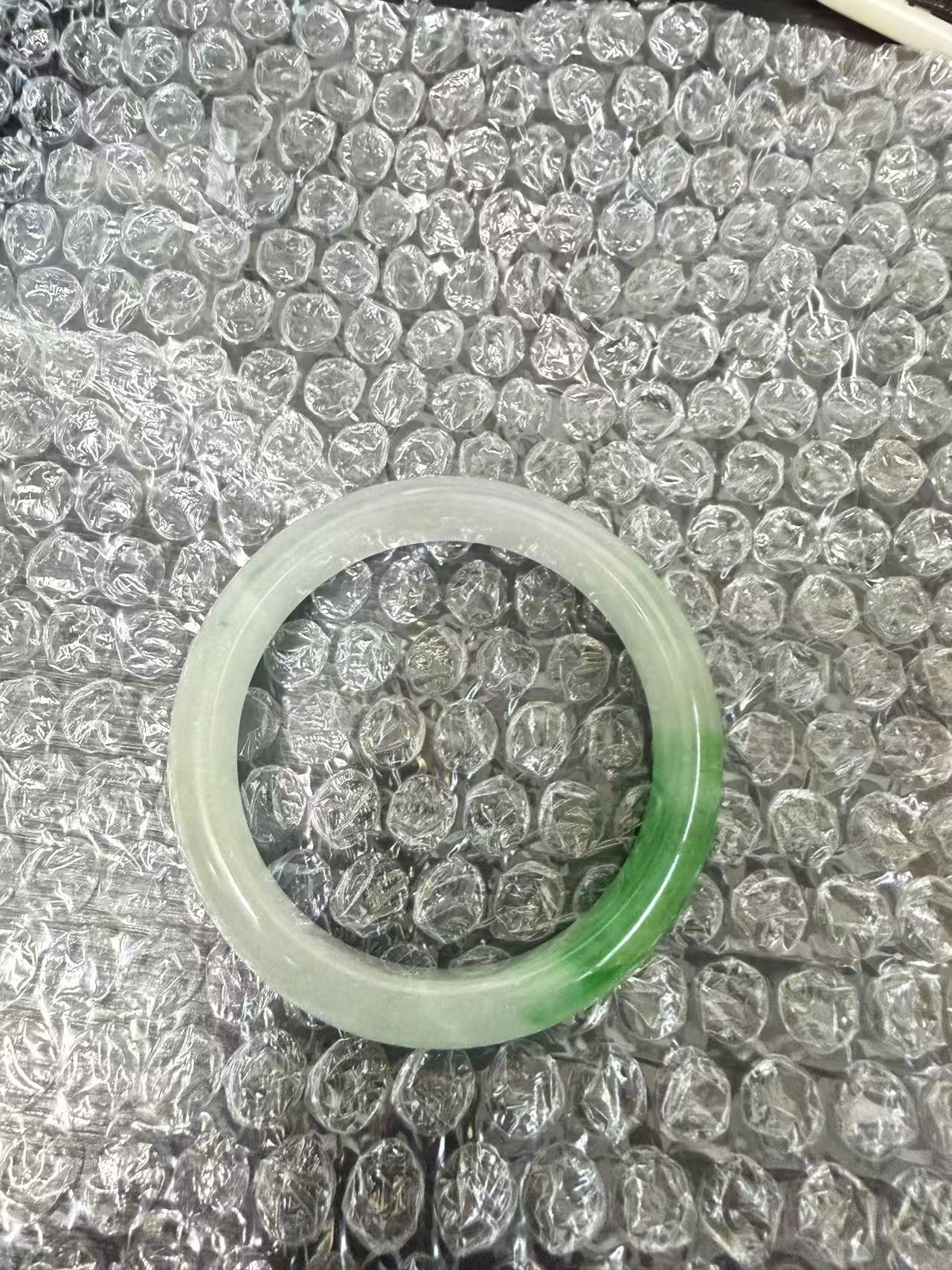 日本代购玉镯开箱图，玉镯放在气泡膜上，展示浅绿到深绿色渐变效果